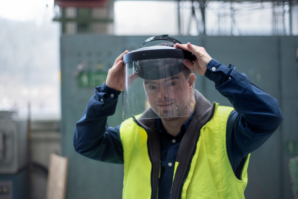 A young man welder with Down syndrome working in industrial factory, social integration concept.