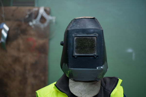 An unrecognizable man welder with helmet working in industrial factory.