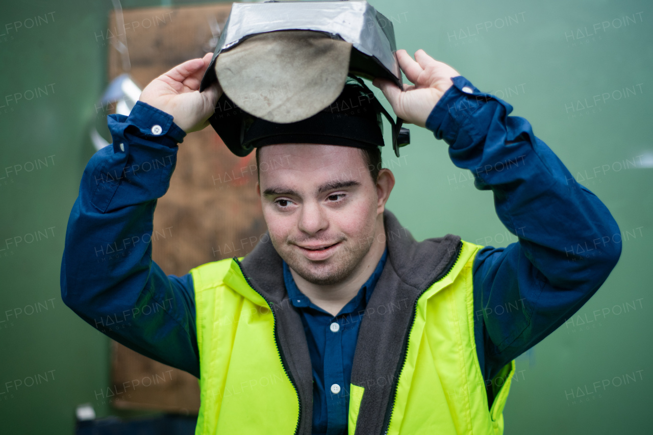 A young man welder with Down syndrome working in industrial factory, social integration concept.