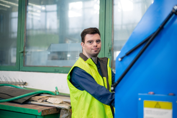 A young man with Down syndrome working in industrial factory, social integration concept.