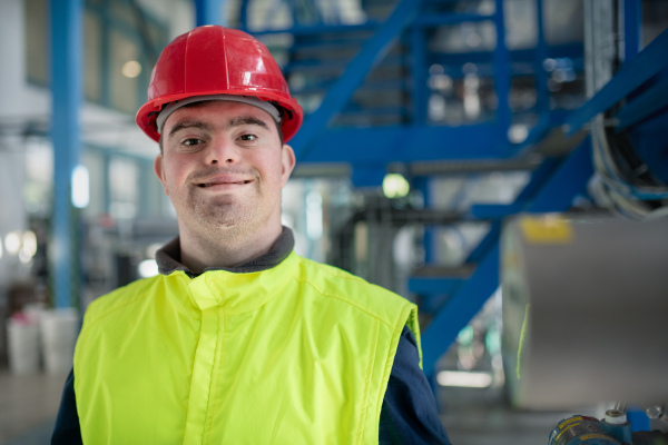 A young man with Down syndrome working in industrial factory, social integration concept.