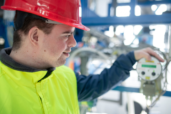 A young man with Down syndrome working in industrial factory, social integration concept.