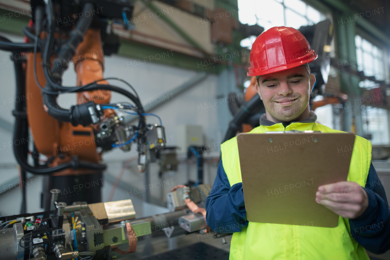 A young man with Down syndrome working in industrial factory,writeing notes, social integration concept.