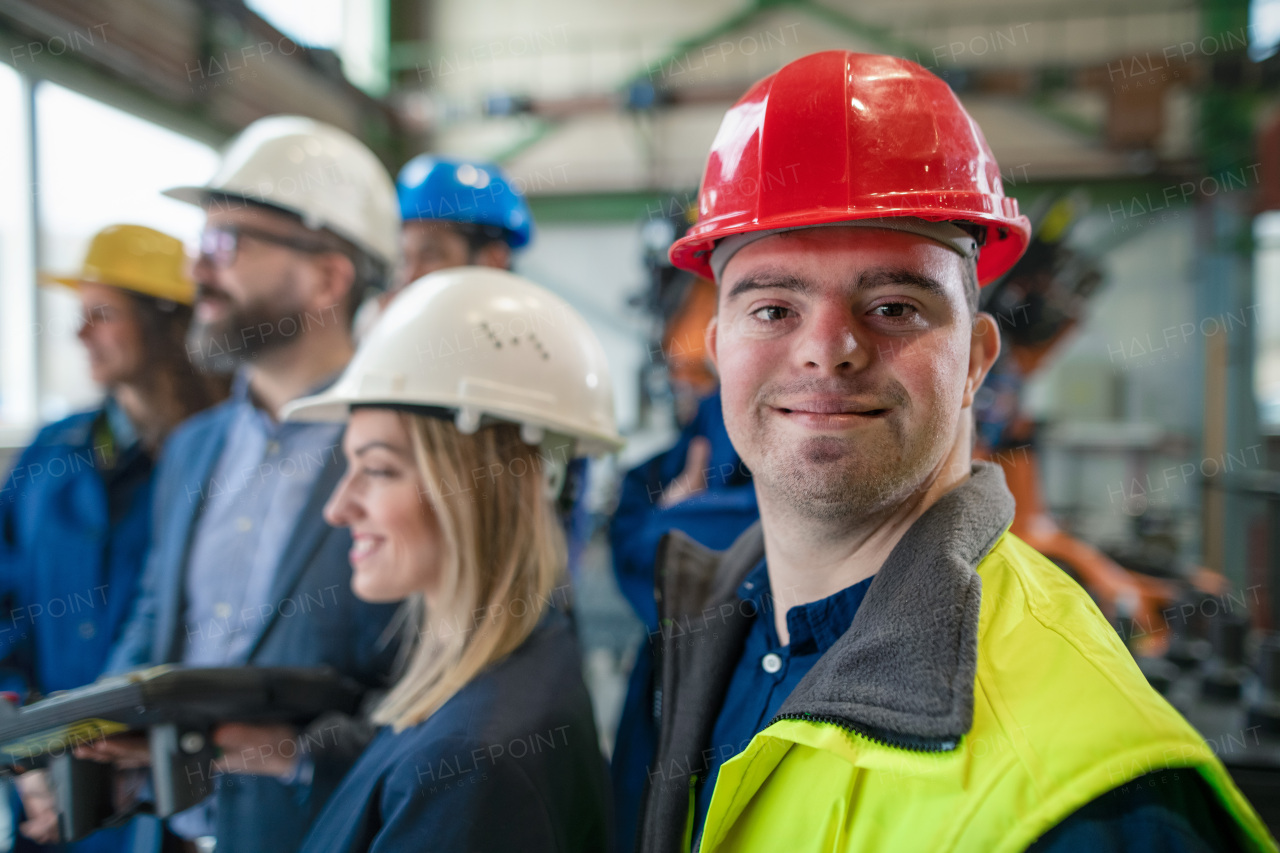 A young man worker with Down syndrome with manager and other collegues working in industrial factory, social integration concept.