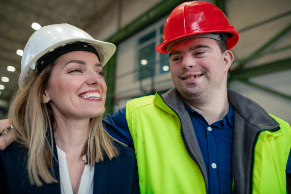 A young man worker with Down syndrome with manager working in industrial factory, social integration concept.