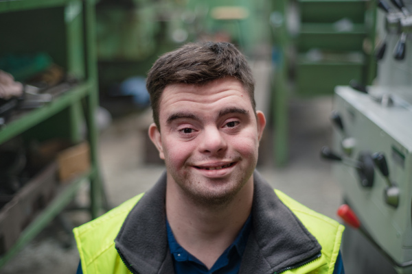 A young man with Down syndrome working in industrial factory, social integration concept.