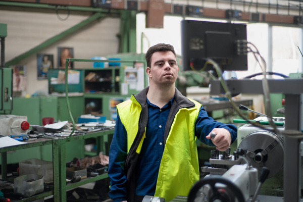 A young man with Down syndrome working in industrial factory, social integration concept.