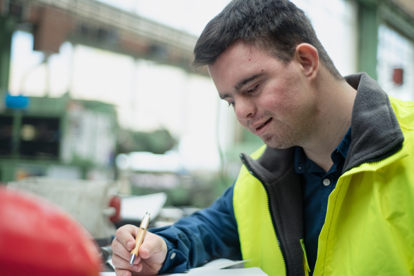 A young man with Down syndrome working in industrial factory, social integration concept.