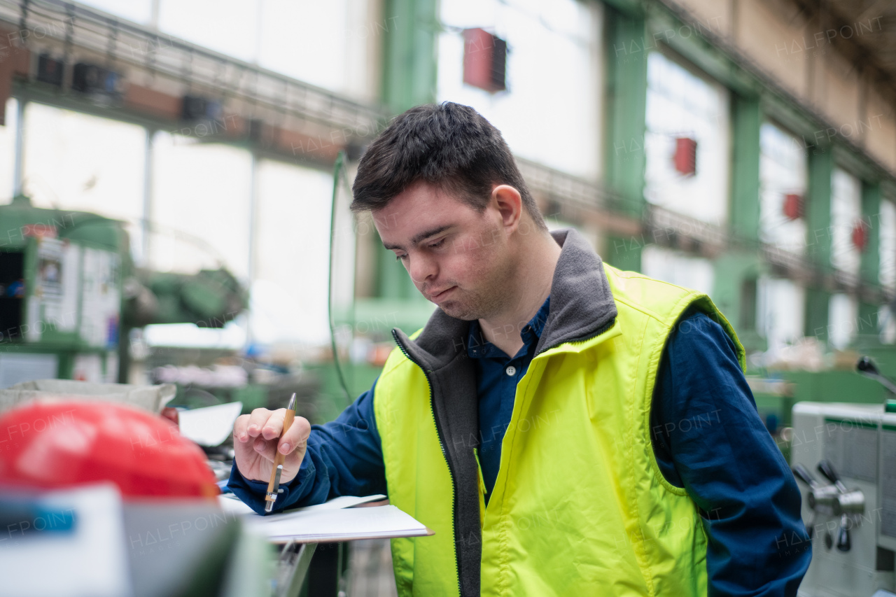 A young man with Down syndrome working in industrial factory, social integration concept.