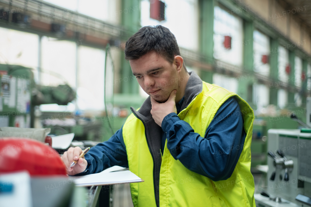 A young man with Down syndrome working in industrial factory, social integration concept.