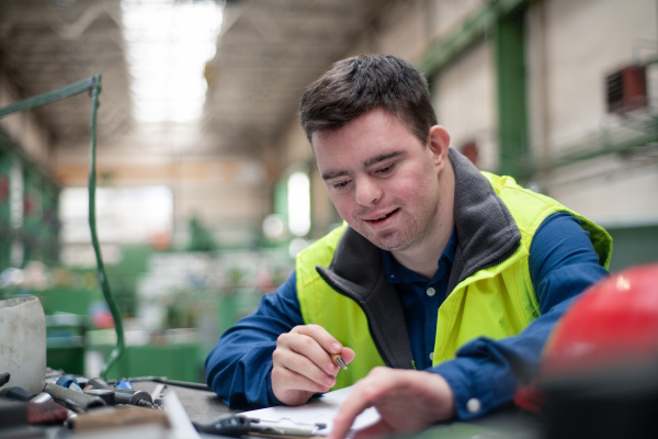 A young man with Down syndrome working in industrial factory, social integration concept.