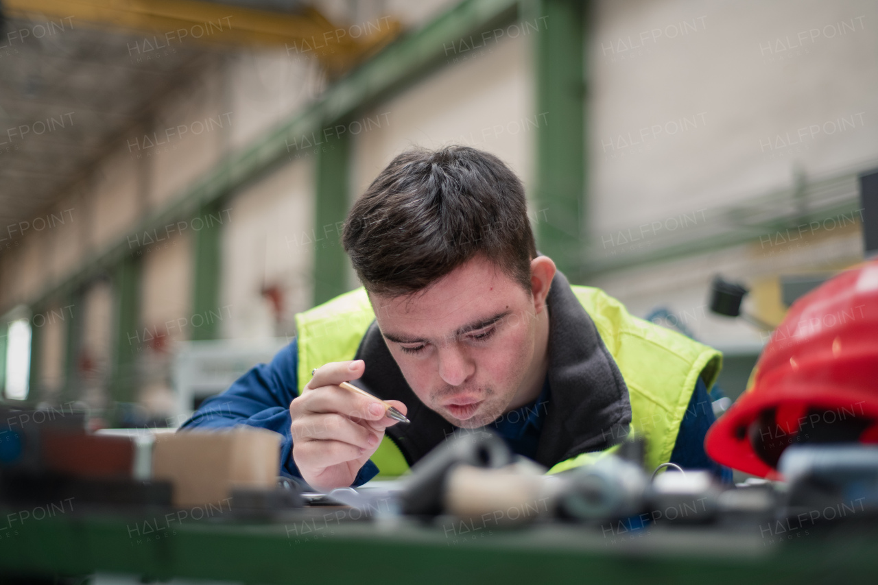 A young man with Down syndrome working in industrial factory, social integration concept.