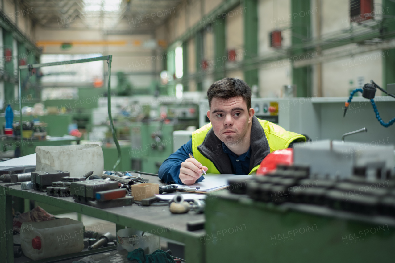 A young man with Down syndrome working in industrial factory, social integration concept.