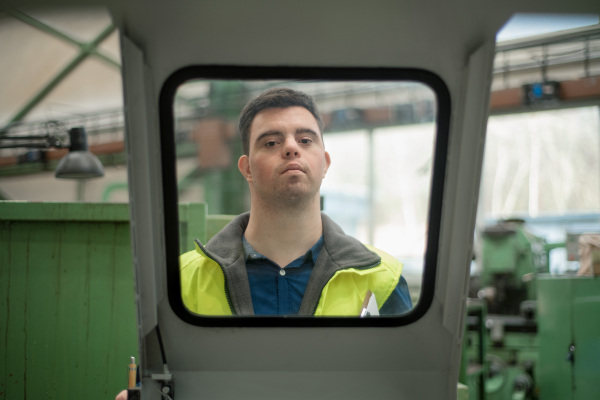 A young man with Down syndrome working in industrial factory, social integration concept.