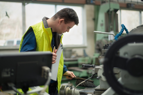 A young man with Down syndrome working in industrial factory, social integration concept.