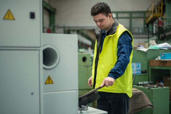 A young man with Down syndrome working in industrial factory, social integration concept.