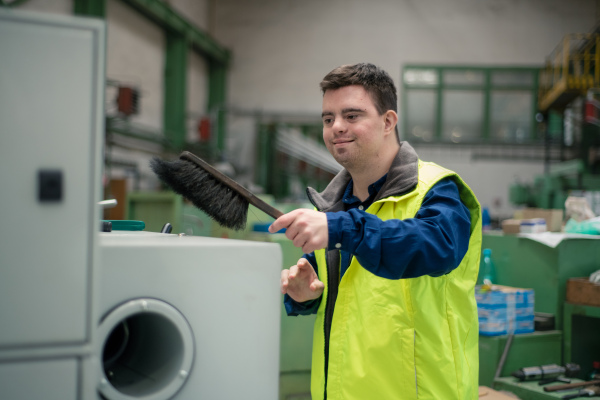 A young man with Down syndrome working in industrial factory, social integration concept.