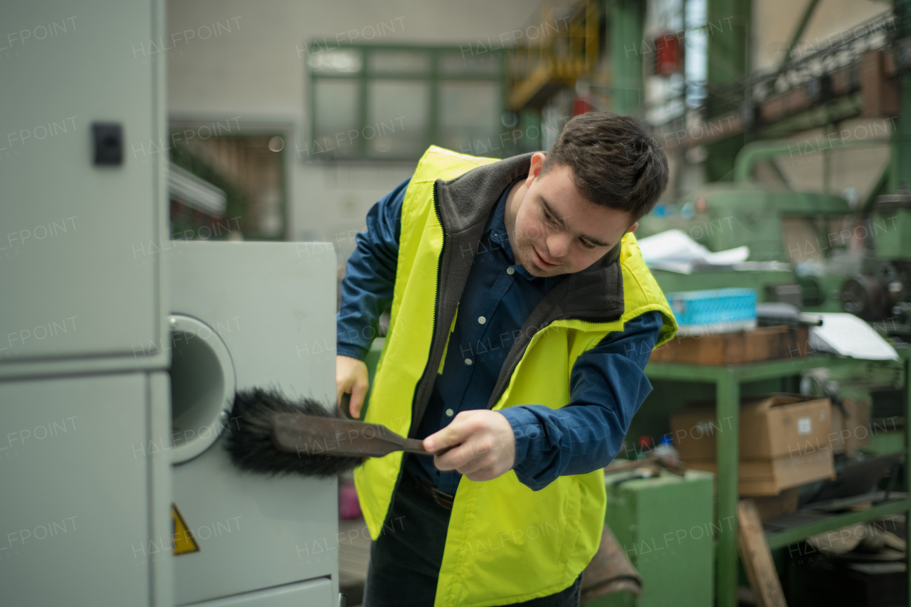 A young man with Down syndrome working in industrial factory,cleaning workspace, social integration concept.