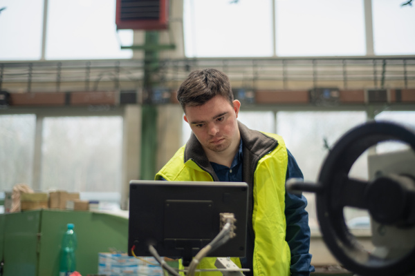 A young man with Down syndrome working in industrial factory, social integration concept.