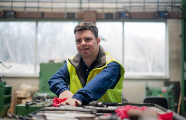 A young man with Down syndrome working in industrial factory, social integration concept.