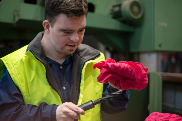 A young man with Down syndrome working in industrial factory, social integration concept.