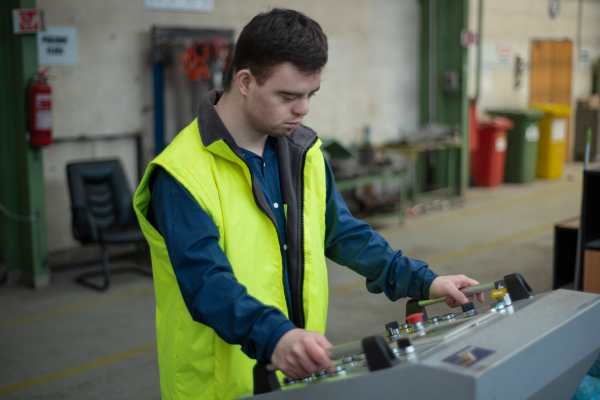 A young man with Down syndrome working in industrial factory, social integration concept.