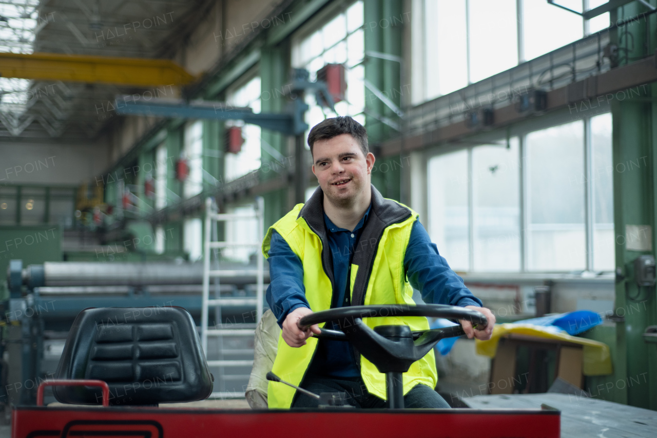 A young man with Down syndrome working in industrial factory,driving working machine, social integration concept.