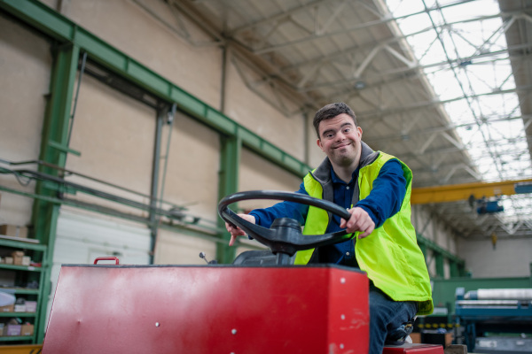 A young man with Down syndrome working in industrial factory, social integration concept.