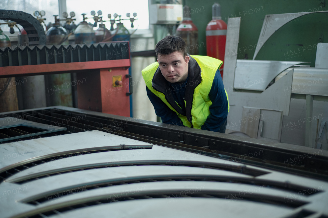 A young man with Down syndrome working in industrial factory,checking finals products, social integration concept.