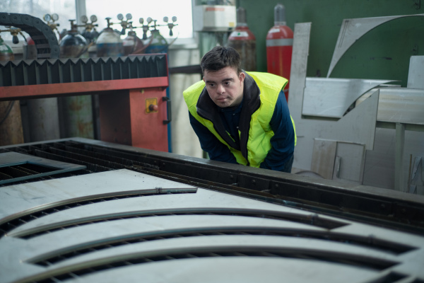 A young man with Down syndrome working in industrial factory,checking finals products, social integration concept.