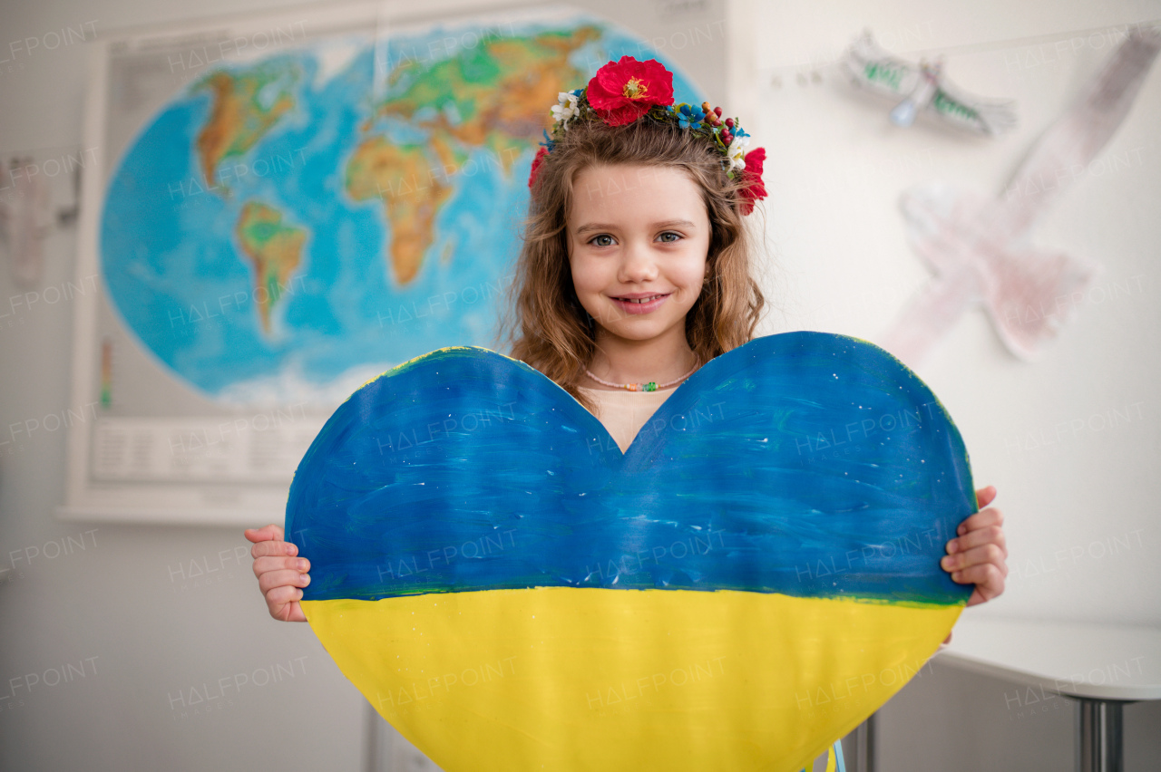 A little Ukrainian schoolgirl holding heart in Ukrainian colors and looking at camera at school.