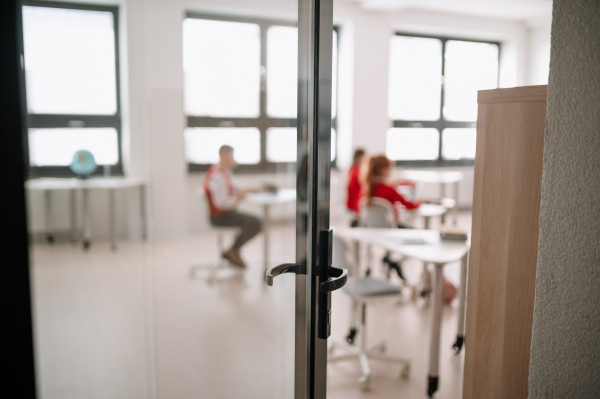 A rear view from open door to class of pupils sitting and listening to teacher in classroom