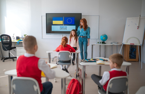 A teacher welcoming Ukrainian schoolgirl in classroom, concept of enrolling Ukrainian kids to schools.