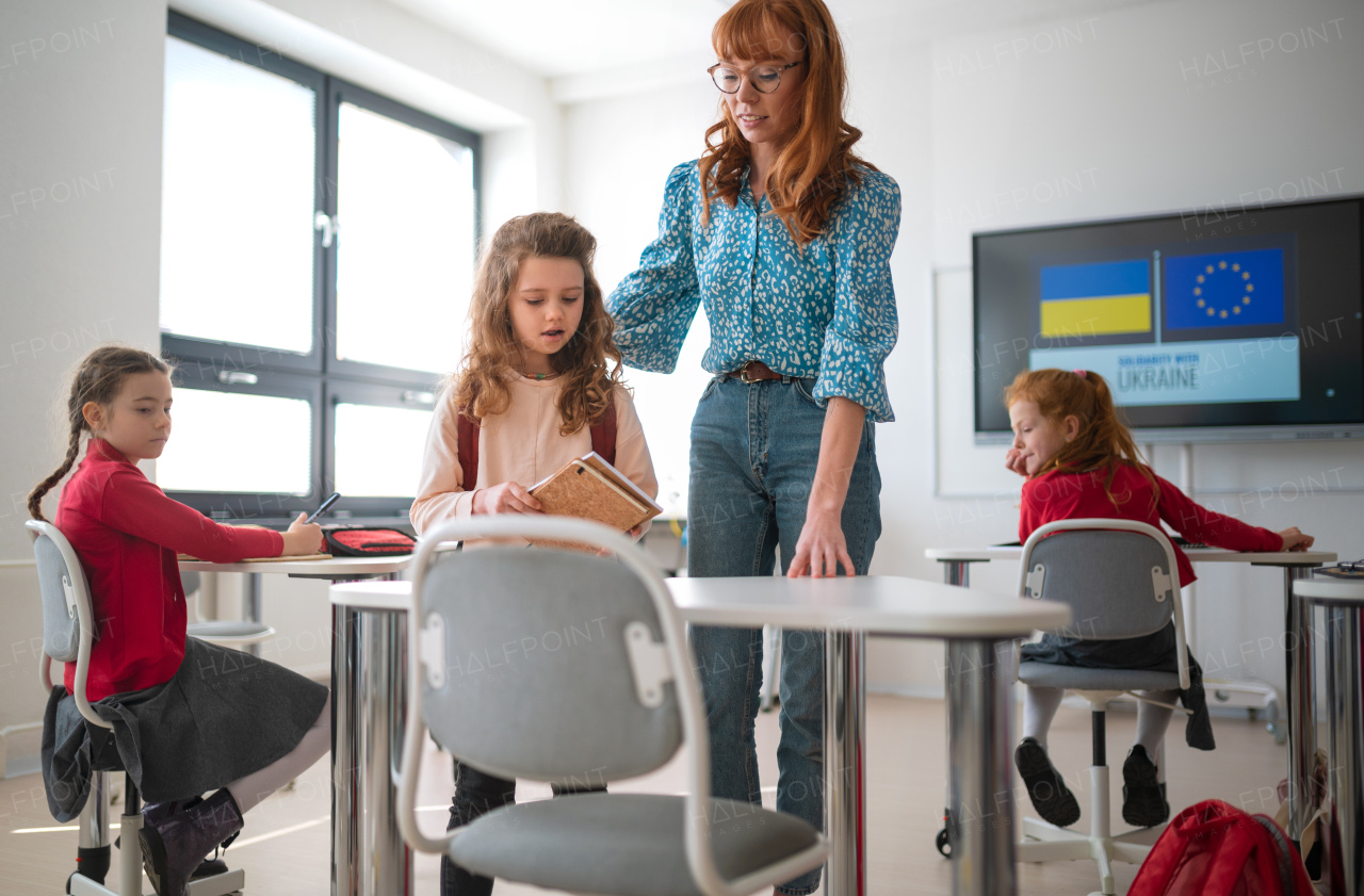 A teacher with Ukrainian schoolgirl in classroom, concept of enrolling Ukrainian kids to schools.