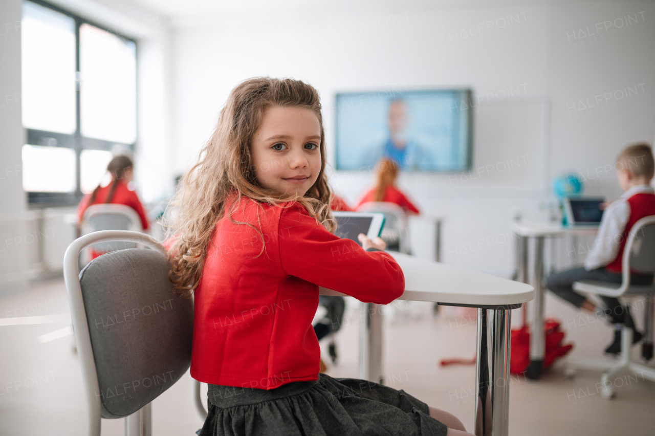 A happy schoolgirl wearing school uniform sitting in class and smiling in the camera.