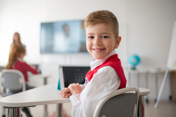 Portrait of happy schoolboy wearing school uniform sitting in class and smiling in the camera.