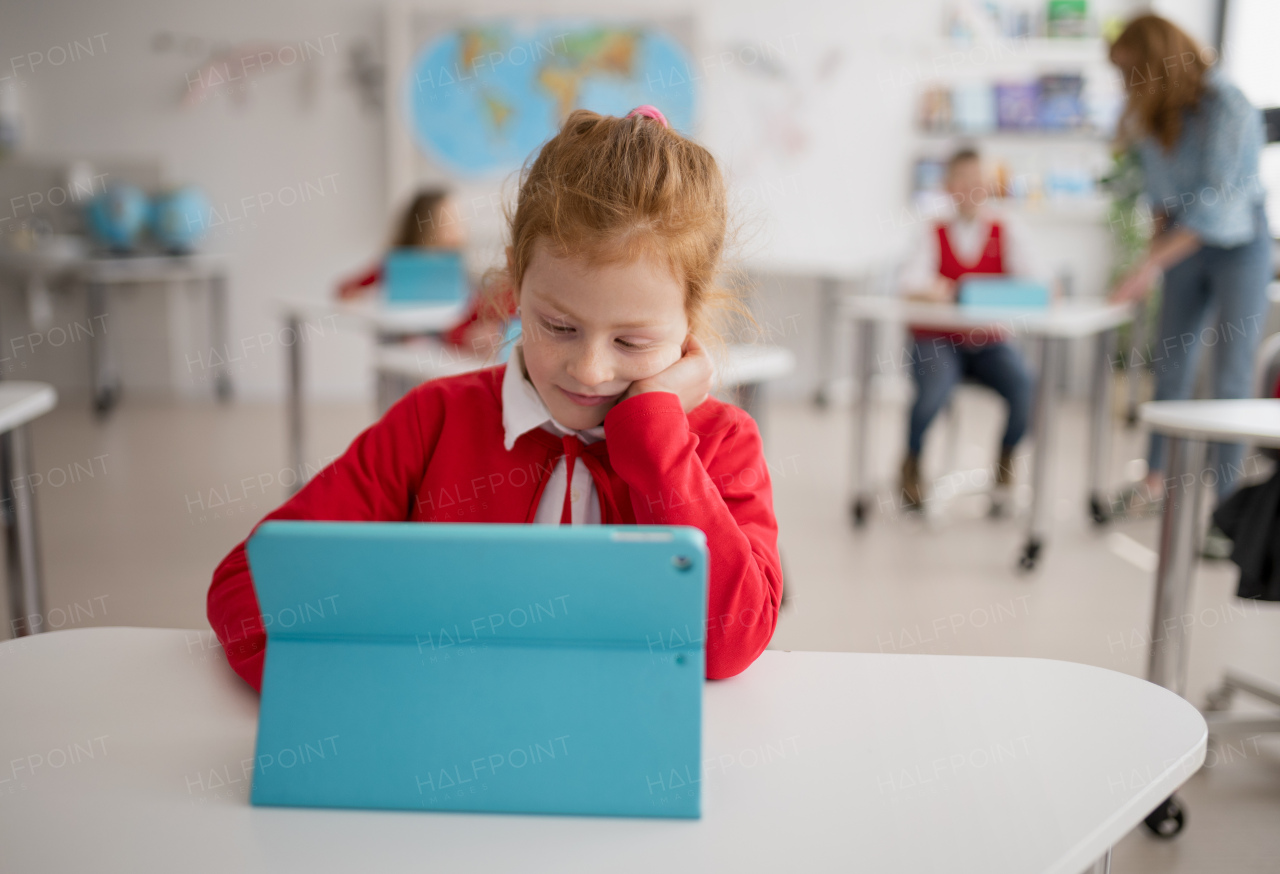 A bored schoolgirl using digital tablet during lesson in classroom at primary school.