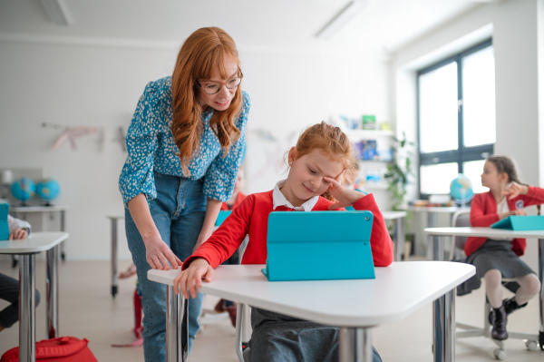 A schoolgirl using tablet with help of teacher during class at school.