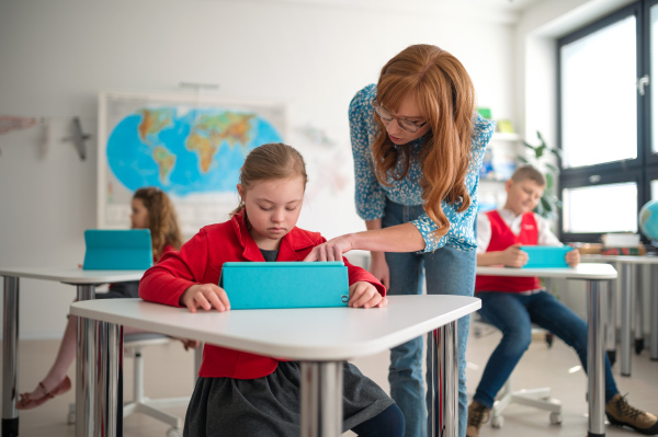 A Down syndrome schoolgirl using tablet with help of teacher during class at school, integration concept.