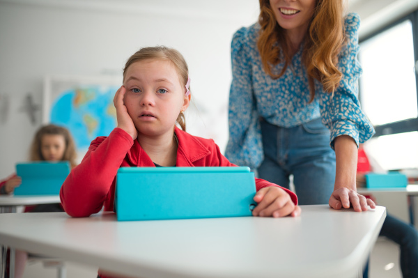 A Down syndrome schoolgirl using tablet with help of teacher during class at school, integration concept.