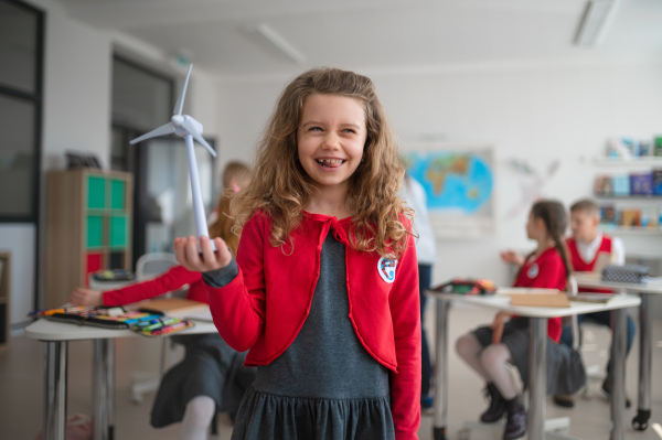 A schoolgirl holding wind turbine and learning about eco-friendly renewable sources of energy in classroom at school