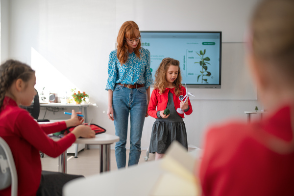 A teacher listening schoolgirl in classroom, science lesson.