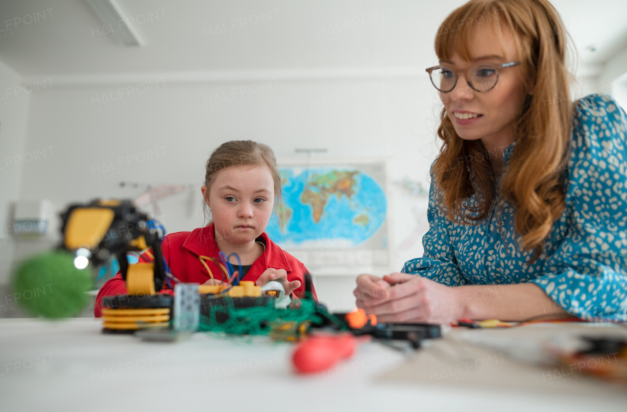 A Down syndrome schoolgirl using robotic arm, learning about robotics with help of teacher during class at school, integration concept.