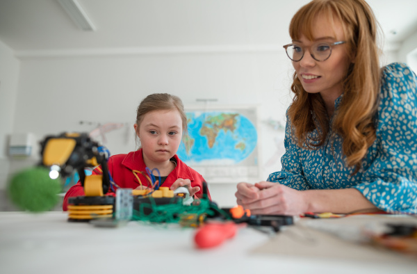 A Down syndrome schoolgirl using robotic arm, learning about robotics with help of teacher during class at school, integration concept.