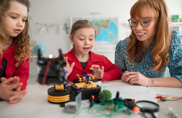 A group of kids with young science teacher programming electric toys and robots at robotics classroom