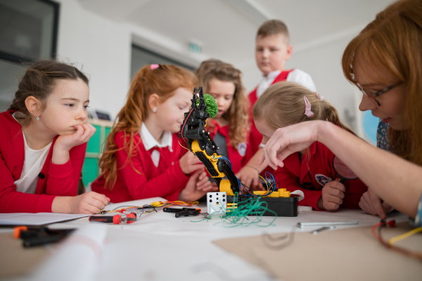 A group of kids with young science teacher programming electric toys and robots at robotics classroom