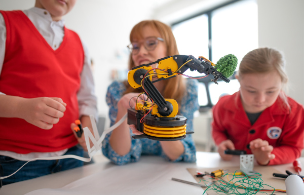 A group of kids with young science teacher programming electric toys and robots at robotics classroom