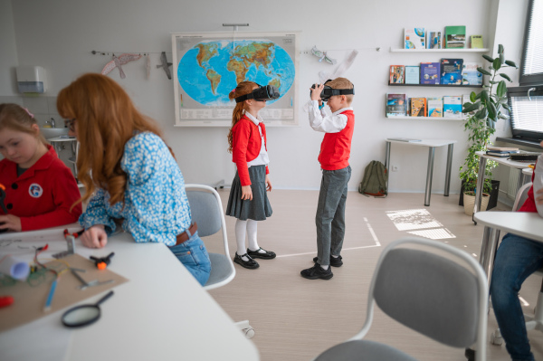 Happy schoolchildren wearing virtual reality goggles at school in acomputer science class