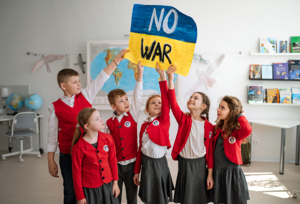 Little schoolchildren holidng and showing an ukrainian flag in classroom, no war concept.