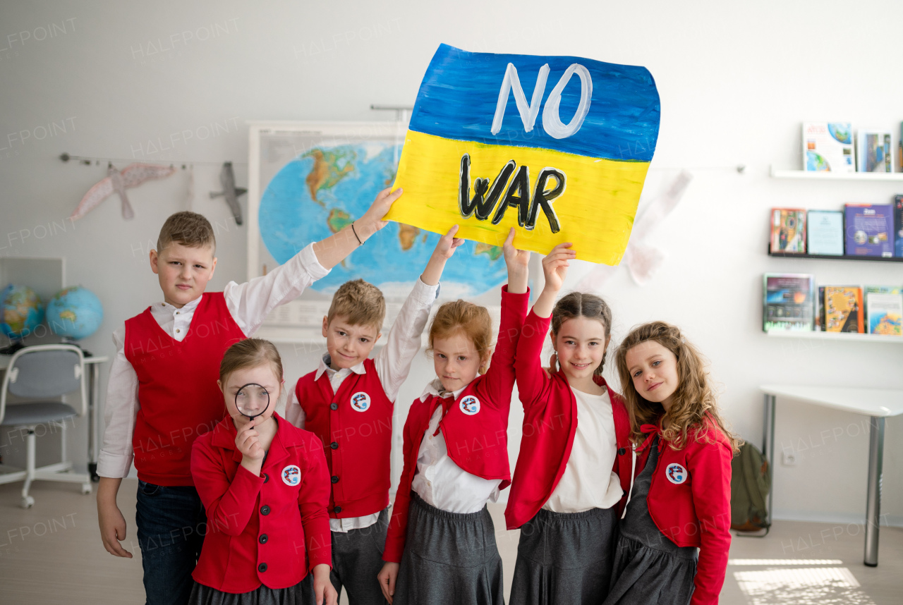 Little schoolchildren holidng and showing an ukrainian flag in classroom, no war concept.